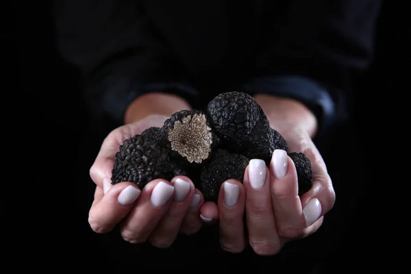 A handful of black truffles in a woman\'s hands. Exquisite and fragrant mushroom. Unrecognizable person. Black background. Close up. Copy space. Top view.