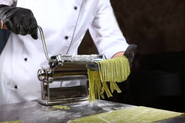 Şef ev yapımı ıspanaklı hamur ile spagetti hazırlıyor. Faydalı bir malzeme. Tanımlanamayan kişi. Siyah arkaplandaki fotoğraf. Boşluğu kopyala.