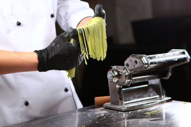 Ispanaklı spagetti için hamur hazırlıyorum. Doğal bileşen. Tanımlanamayan kişi. Karanlık arka plan. Makarna pişirme makinesi. Ev yemeği kavramı.