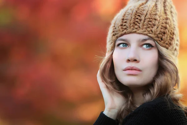 Portrait of a girl in a knitted hat. Handmade hats. Woman\'s portrait on a background of autumn trees. Warm clothes. Autumn season. Copy space.