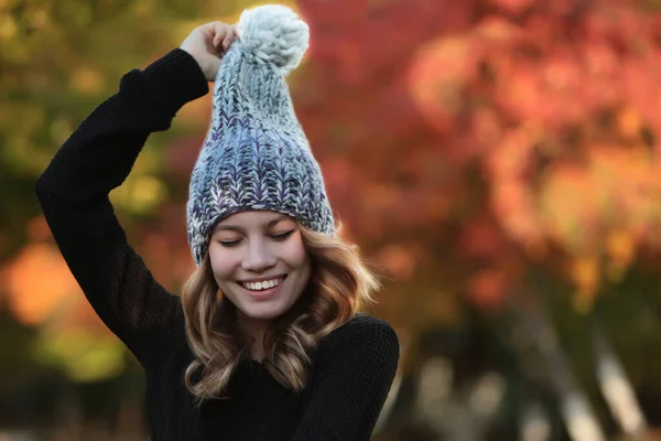 A young girl in a warm knitted hat. The girl closed her eyes and holds a pompon or brush in her hand. Handmade hats. Warm clothes. Autumn season. Copy space.