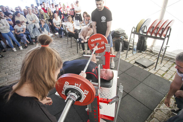 Russia, Moscow - June 2, 2018: Powerlifting competition. Brutal athletic man pumping up muscles on bench press with assistant. Sportsman is engaged in the gym. 