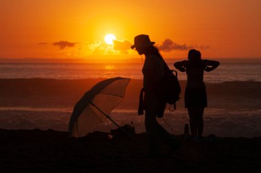 Şapkalı genç bir kadın, oğluyla kumsalda gün batımını seyrediyor. Arka planda Pasifik Okyanusu ve kızıl gökyüzü. Şili 'nin merkez kıyısı, Güney Amerika