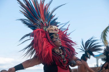 Geleneksel kostümlü, tüylü, alnında kafatası olan bir Maya kadını kabile dansında dans ediyor. Arka planda diğer Maya dansçıları