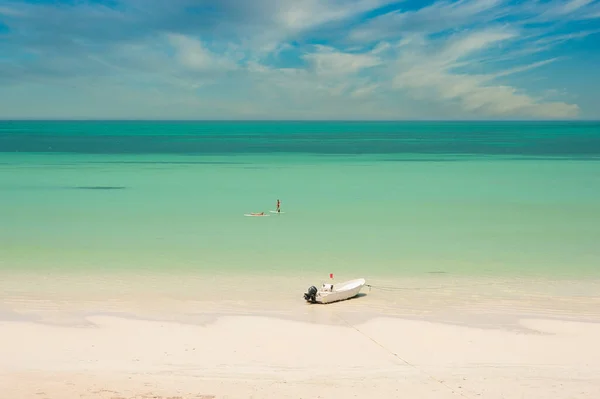 İki genç kadın, Meksika 'daki Holbox Adası' nda beyaz bir kumsalda sörf yaparken dinleniyor. Terkedilmiş sahilde kıyıya demirlemiş küçük bir tekne ve arka planda Karayip Denizi..