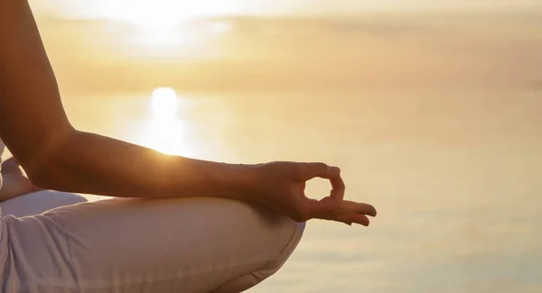 El concepto de meditación. Parte del cuerpo de una mujer en la posición de loto, mudra dedo contra la puesta del sol y el mar tranquilo . Fotos de stock