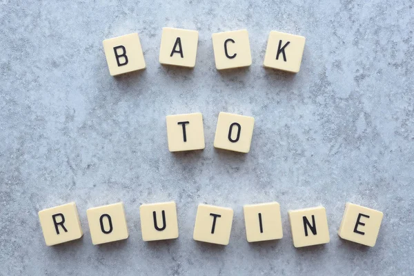 Back to routine message text formed by game tiles and placed on a grey flecked stone background. Tabletop.