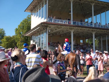 İnsanlar yarış atı Songo ve jokey Fabian Xaver Weissmeier 'i alkışlıyor. Tribünlere bakın. Iffezheim Racetrack, Baden-Baden, Almanya. Yaz, mavi gökyüzü.