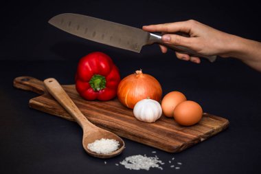 Kapsiyum, soğan, sarımsak gibi, akasya tahtasının üzerinde, pirinç ile ahşap bir kaşık ve siyah bir arka planda yumuşak bir deseni olan patates gibi sebzelerin ön fotoğrafı.. 