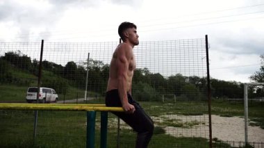 Spor alanında paralel barlarda karın kaslarını çalıştıran güçlü bir adam. Genç üstsüz sporcu doğada egzersiz yapıyor. Doğada spor yapan sporcu. Aktif spor yaşam tarzı kavramı.