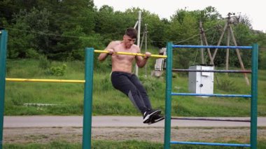 Güçlü ve kaslı bir adam doğanın yatay çubuğunda egzersiz yapıyor. Spor sahasında sıkı gömleksiz sporcu. Genç atletik adam dışarıda egzersiz yapıyor. Sağlıklı yaşam tarzı kavramı.