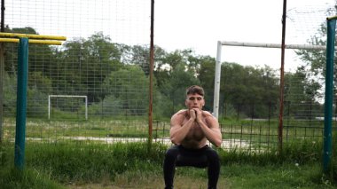 Spor sahasında çömelme hareketleri yapan erkek üstsüz atlet. Yaz doğasında çalışan genç bir sporcu. Güçlü sporcu dışarıda egzersiz yapıyor. Aktif ve sportif yaşam tarzı kavramı. Yavaş çekim