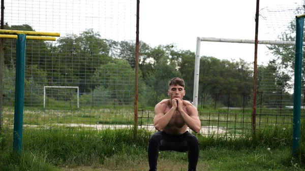 Spor sahasında çömelme hareketleri yapan erkek üstsüz atlet. Yaz doğasında çalışan genç bir sporcu. Güçlü sporcu dışarıda egzersiz yapıyor. Aktif ve sportif yaşam tarzı kavramı. Yavaş çekim