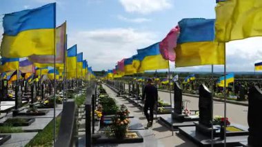 Mourning man go among countless graves of ukrainian soldiers with national flags at military cemetery in Kharkiv. Scene reflects personal sorrow and nation collective loss caused by russian aggression.