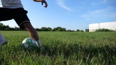 Profesyonel futbolcunun erkek ayağı, yeşil sahada koşarken topla numaralar gösterir. Güneşli bir günde Meadow 'da koşan sporcu bacakları topa vurur. Stadyumda antrenman yapan genç adam. Yavaş çekim