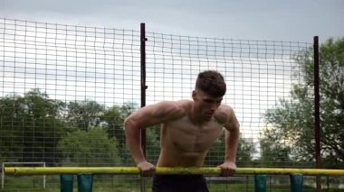 Erkek üstsüz sporcu doğada paralel barlarda şınav çekiyor. Spor alanında egzersiz yapan güçlü bir sporcu. Genç sporcu dışarıda sıkı çalışıyor. Aktif spor yaşam tarzı kavramı. Yavaş çekim