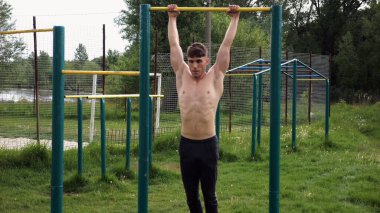 Spor sahasında barfiks çeken kaslı bir sporcu. Genç üstsüz sporcu doğada egzersiz yapıyor. Güçlü sporcu adam dışarıda antrenman yapıyor. Sağlıklı ve aktif yaşam tarzı kavramı. Yavaş çekim