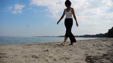 Güneşli bir günde sahilde kumsala giden mutlu yetişkin kadın. Arka planda sakin dalgalarla deniz kıyısında yürüyen güzel bir bayan. Yaz tatili ya da tatil kavramı. Yavaş çekim