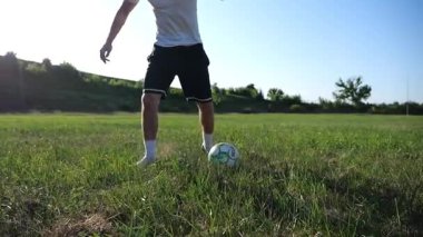 Profesyonel futbolcunun erkek ayağı, yeşil sahada koşarken topla numaralar gösterir. Güneşli bir günde Meadow 'da koşan sporcu bacakları topa vurur. Stadyumda antrenman yapan genç adam. Yavaş çekim