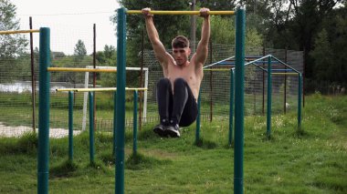 Spor sahasında karın kaslarını çalıştıran güçlü bir adam. Genç sporcu, barfiks çekme çubuğunda egzersiz yapıyor. Doğada spor yapan sporcu. Sportif yaşam tarzı kavramı.