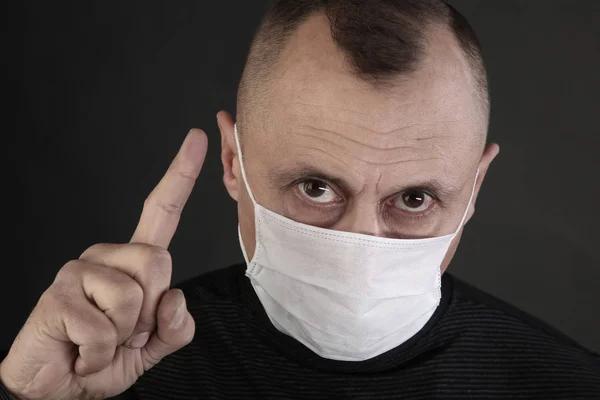 closeup portrait man in a black T-shirt and a medical mask on a gray background studio