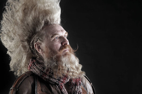 Портрет харизматичного взрослого мужчины с бородой и высоким ирокезом в студии на тёмном фоне
 