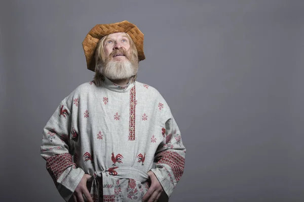 Slavic bearded man in a beautiful painted shirt and a birchbark hat