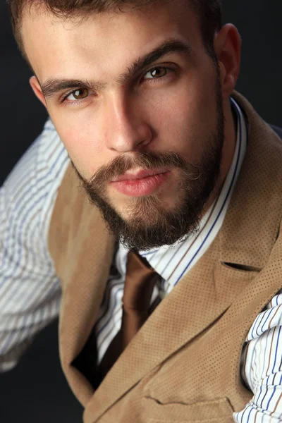 closeup portrait of the beautiful charismatic young man with a beard wearing pants, shirt, vest and tie on a dark background studio