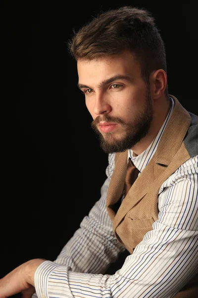 closeup portrait of the beautiful charismatic young man with a beard wearing pants, shirt, vest and tie on a dark background studio