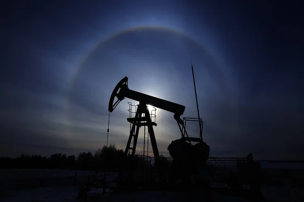 closeup of an oil pump in a snowy field near a forest in the sunlight halo