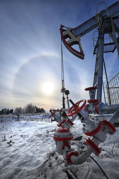 closeup of an oil pump in a snowy field near a forest in the sunlight halo