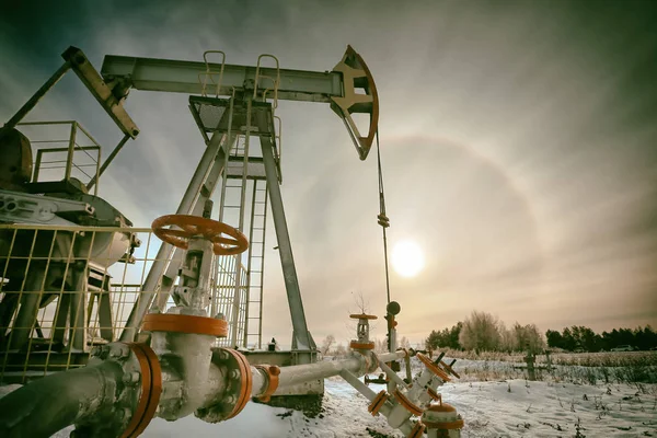 closeup of an oil pump in a snowy field near a forest in the sunlight halo