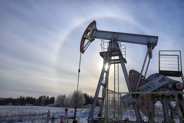 closeup of an oil pump in a snowy field near a forest in the sunlight halo