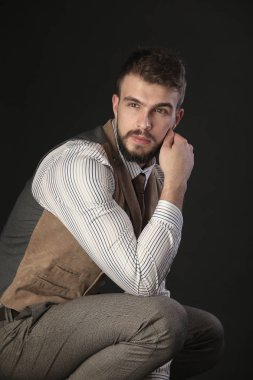 portre portre sakal giyen ile güzel karizmatik genç adamın pantolon, gömlek, yelek ve bir koyu arka plan stüdyo kravat