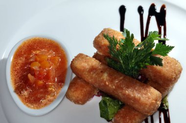 Balık kroketi, sebzeli ve soslu beyaz tabakta.