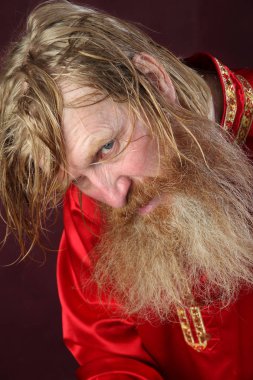 Kırmızı gömlek stüdyosunda uzun sakallı, bıyıklı ve ıslak sarı saçlı kutsanmış birinin yakın plan portresi.
