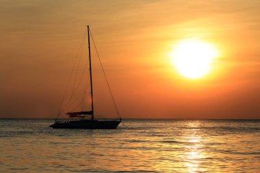 Deniz manzaralı gün batımı ve Tayland kıyılarında sönük yelkenli bir tekne.