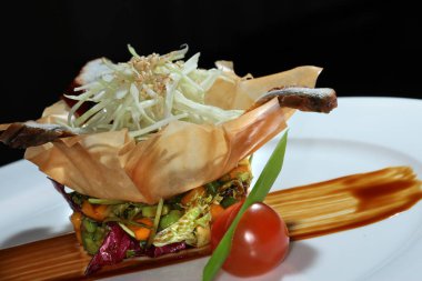 Siyah arka plan stüdyosunda hamurdan yapılmış bir sepetin içinde balık ve sebzeli yakın plan gurme salatası.