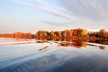 Sonbahar manzarası nehirde güzel bir sabah kumsalda renkli ağaçlar ve mavi gökyüzünde bulutlar.