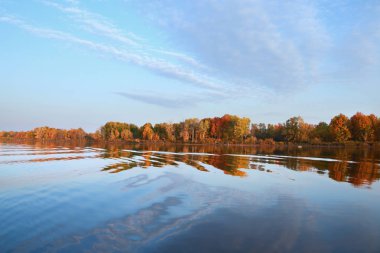 Sonbahar manzarası nehirde güzel bir sabah kumsalda renkli ağaçlar ve mavi gökyüzünde bulutlar.