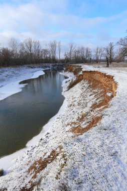 Güneşli bir kış günü, dondurucu nehrin ve yapraksız meşe ağaçlarının resimsel manzarası.