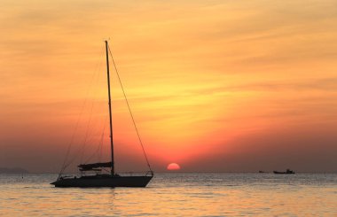 Deniz manzaralı gün batımı ve Tayland kıyılarında sönük yelkenli bir tekne.