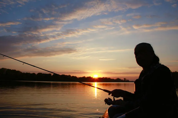 Portrait of a man in profile in a boat on a river with a fishing pole in his hands at sunset in autumn