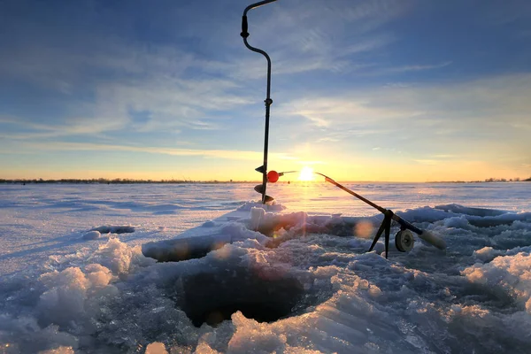 クローズ アップ ドリル 夕暮れ時の冬の川の氷の上の穴の付近の釣り竿 — ストック写真