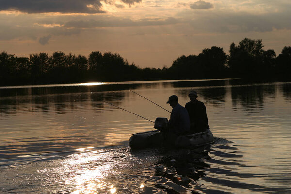 Двое мужчин отправляются на рыбалку с лодки на реке на закате в конце лета
