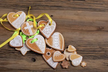  Sarı kurdeleli kalp şeklinde makro zencefilli kurabiye, ahşap arka planda çiçekler.