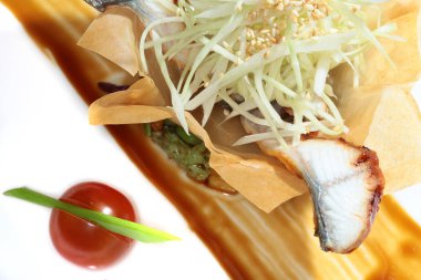 Siyah arka plan stüdyosunda hamurdan yapılmış bir sepetin içinde balık ve sebzeli yakın plan gurme salatası.