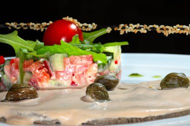 Kapari, taze otlar ve krema sosuyla süslenmiş, siyah bir arka plan stüdyosundaki beyaz tabakta çok güzel dekore edilmiş.