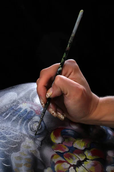 close-up artist\'s hand on the body art on a black background studio