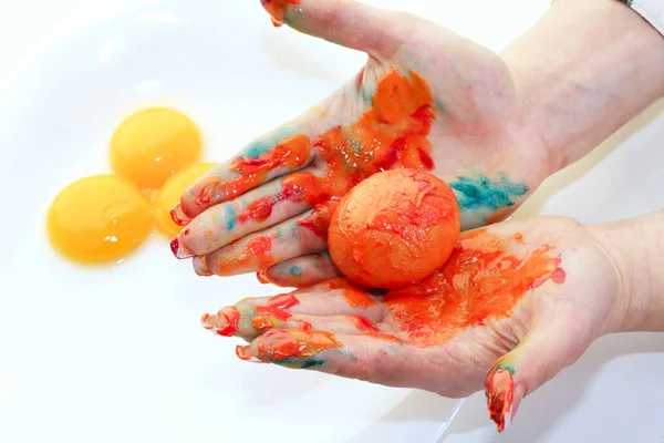 close-up of a single egg in the orange paint in female hands on a light background studio